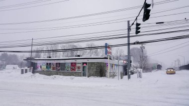 NORWALK, CT, ABD - 23 Şubat 2026: Bir sokak kavşağındaki küçük bir binaya ağır kar yağar. Bölge beyazlarla kaplı ve araçlar karda hareket ediyor. Elektrik hatları sahne boyunca uzanıyor..