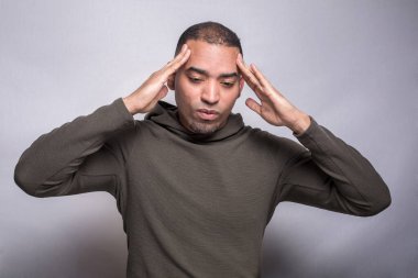 Latin kökenli bir adam el ele tutuşup şakaklarına bastırıyor. Baş ağrısı çekiyor. Gri arka planda izole edilmiş.