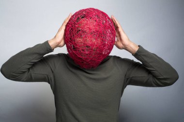 Kafasında büyük örgü bir maske tutan bir adam, gri arka planda soyutlanmış.