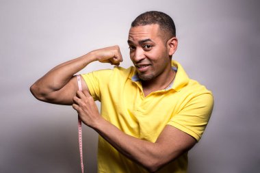 Latin bir Latin 'in portresi, kaslarını bantla ölçen, gülümseyen, gri üzerine izole edilmiş siyah bir adam. 