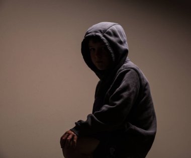 A dark portrait of a faceless child in the hoodie, sitting on a chair, silhouette in the dark environment clipart