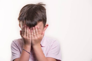 Beyaz arka planda izole edilmiş polo tişört giyen, yüzünü saklayan beyaz bir çocuğun portresi.