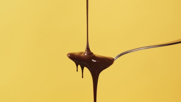 Flusso di cioccolato liquido fuso in primo piano, cucchiaio da pasticceria in metallo ricoperto da un flusso di cioccolato fluente o salsa al caramello marrone su sfondo giallo. Cottura dolce dessert al cioccolato e caramelle. Prodotti da forno — Video Stock