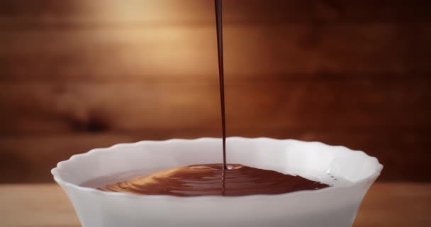 근접녹인 뜨거운 액체 초콜릿은 부엌에 있는 나무 배경 위에 하얀 그릇에 담겨 녹은 우유 초콜릿이나 갈색 캐러멜 소스를 붓는다. 손으로 만든 초콜릿 디저트와 사탕 요리 — 비디오