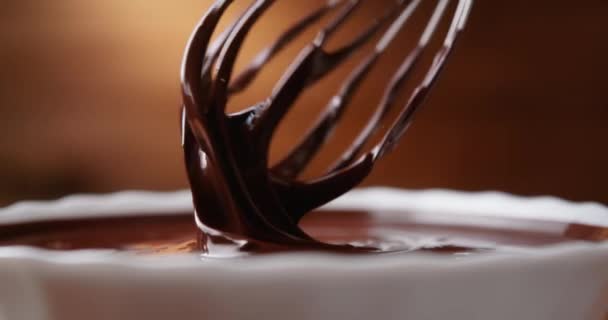 Primer plano chocolatero mezclando chocolate líquido derretido con batidor de acero. Mezcla de chocolate caliente y remolino en un tazón blanco sobre fondo de madera. Cocinar postre de chocolate hecho a mano. Concepto de confitería — Vídeo de stock