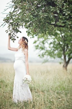 Yaz park zevk, uzun beyaz elbise giyiyordu, eller buket çiçek, açık havada, içinde yeni yaşam konsepti holding hamile kadın. taze ruh hali