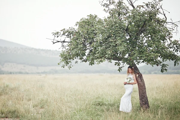 Mulher grávida desfrutando de parque de verão, vestindo vestido branco longo, segurando em mãos buquê de flores, ao ar livre, novo conceito de vida. humor fresco — Fotografia de Stock