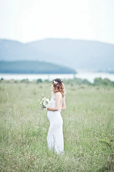 Mulher grávida desfrutando de parque de verão, vestindo vestido branco longo, segurando em mãos buquê de flores, ao ar livre, novo conceito de vida. humor fresco — Fotografia de Stock