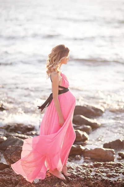 Schwangere in rosa Kleid am Strand am Meer — Stockfoto