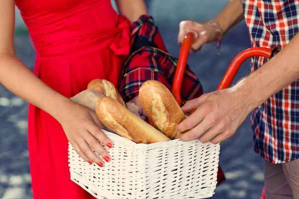 Man's and woman's hands near red bicycle in park with tasty bread in basket — Stock Photo, Image