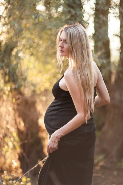 Zwangere vrouw met lang blond haar poseren in zonnig park. jonge — Stockfoto