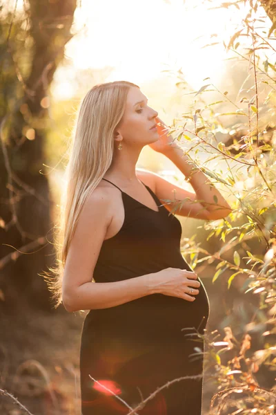 Zwangere vrouw met lang blond haar poseren in zonnig park. jonge — Stockfoto
