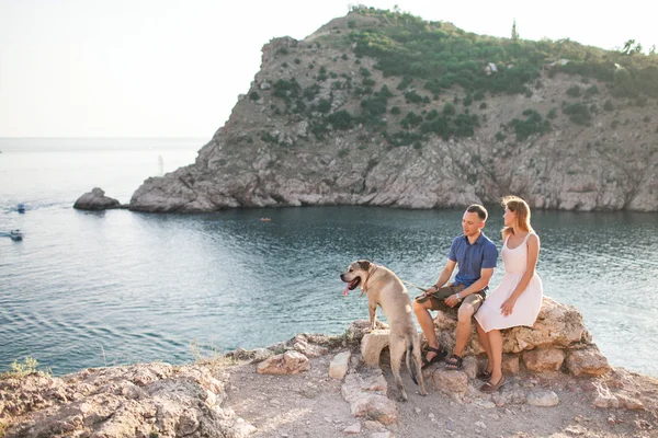 Par killar leker med sin hund på berget nära havet. Romantisk tid i naturen med vacker utsikt. — Stockfoto