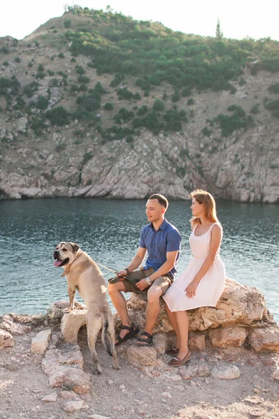 Par killar leker med sin hund på berget nära havet. Romantisk tid i naturen med vacker utsikt. — Stockfoto