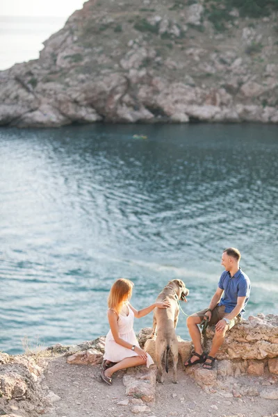 Couple of guys playing with their dog on the mountain near ocean. Romantic time in nature with beautiful view. — Stock Photo, Image