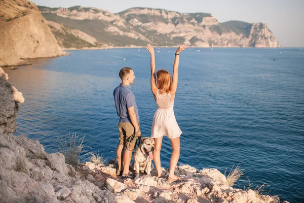 Par killar leker med sin hund på berget nära havet. Romantisk tid i naturen med vacker utsikt. — Stockfoto