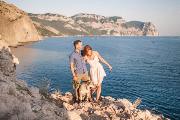 Un par de tipos jugando con su perro en la montaña cerca del océano. Tiempo romántico en la naturaleza con hermosa vista . —  Fotos de Stock