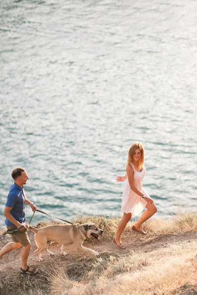 Couple of guys playing with their dog on the mountain near ocean. Romantic time in nature with beautiful view. — Stock Photo, Image