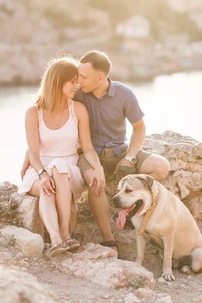 Couple of guys playing with their dog on the mountain near ocean. Romantic time in nature with beautiful view.