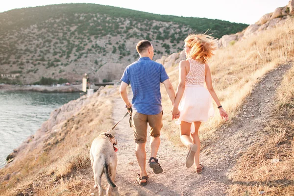 Couple of guys playing with their dog on the mountain near ocean. Romantic time in nature with beautiful view. — Stock Photo, Image