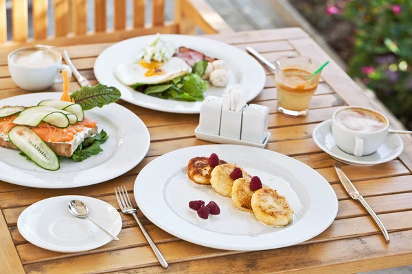 Lekker ontbijt. kaastaart, broodje met gerookte zalm, gebakken eieren met bacon en koffie — Stockfoto