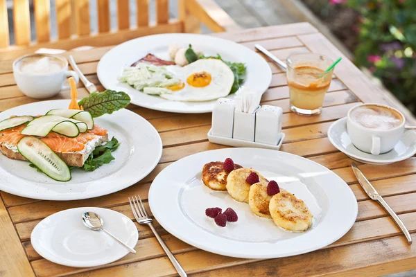 Lekker ontbijt. kaastaart, broodje met gerookte zalm, gebakken eieren met bacon en koffie — Stockfoto