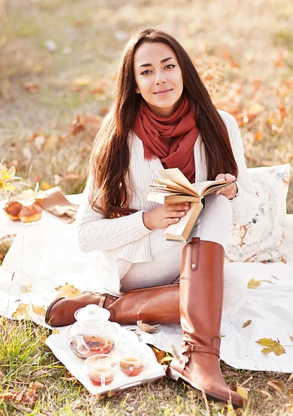 Young beautiful brunette drink tea and read book in the autumn park — Stock Photo, Image