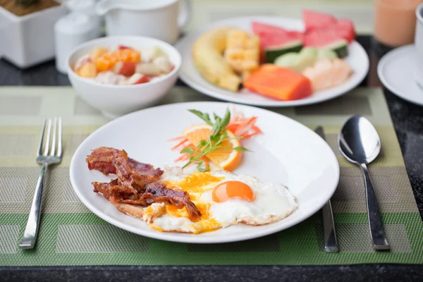 Hotel breakfast. Fried eggs with bacon and fruit — Stock Photo, Image