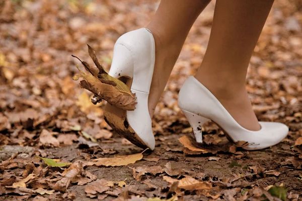 Pernas de mulher em sapatos brancos com folhas marrons — Fotografia de Stock