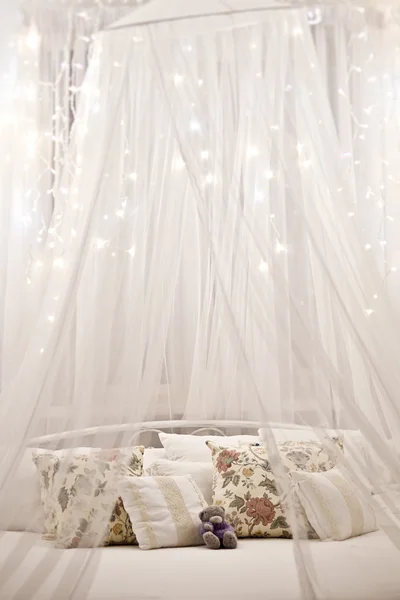 Cama blanca y acogedora con almohada vintage y luces de Navidad —  Fotos de Stock