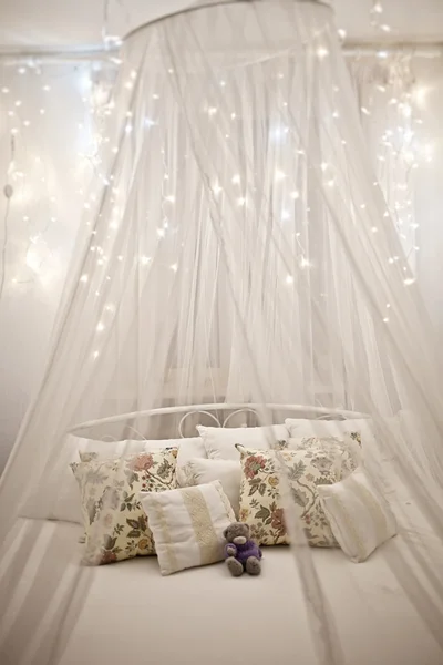 Cama blanca y acogedora con almohada vintage y luces de Navidad —  Fotos de Stock