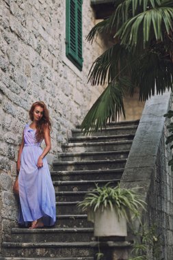 Genç güzel kız portresi uzun elbise eski şehirde sokakta yürürken uçan solgun Lila renkli moda