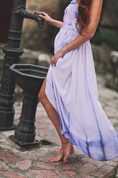 Portret van jonge mooi meisje mode in bleke lila kleur lang vliegen jurk lopend onderaan de straat in de oude stad — Stockfoto