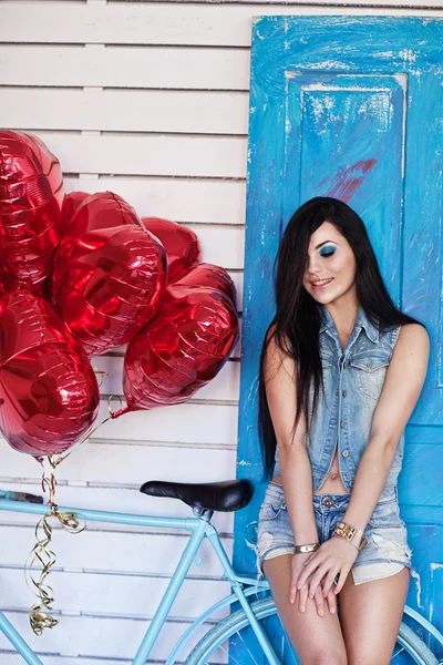 Schöne brünette junge Frau in Jeans mit herzförmigen Luftballons in der Nähe von Fahrrad. Valentinstag. — Stockfoto