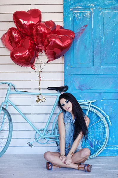 Vacker brunett ung kvinna i jeans med en Hjärtformade ballonger nära cykel. Alla hjärtans dag. — Stockfoto
