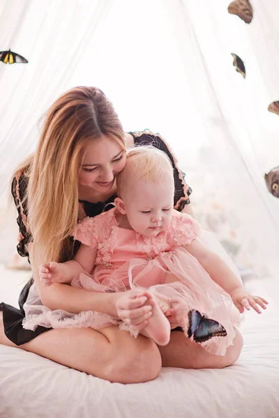 Mooie jonge vrouw met kleine dochter zittend op de witte bed met vlinder. — Stockfoto