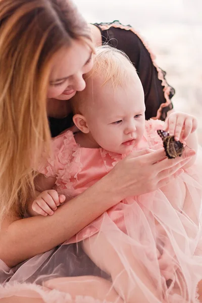 Mooie jonge vrouw met kleine dochter zittend op de witte bed met vlinder. — Stockfoto