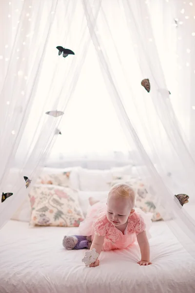 Mooi klein meisje met vlinders rondom witte bed. — Stockfoto