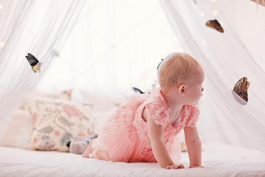 Pretty little girl with butterflies all around white bed.