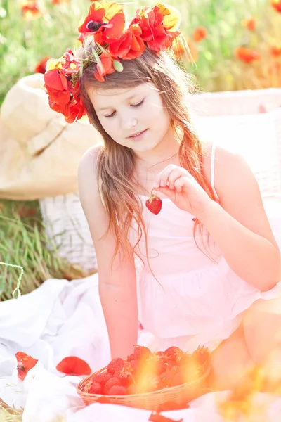 Piccola ragazza in ghirlanda di papavero mangiare fragola nel campo. Picni — Foto Stock