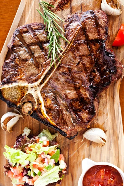 Клубний яловичий стейк з перцевим соусом та овочами на ріжучій дошці на темному дерев'яному фоні — стокове фото