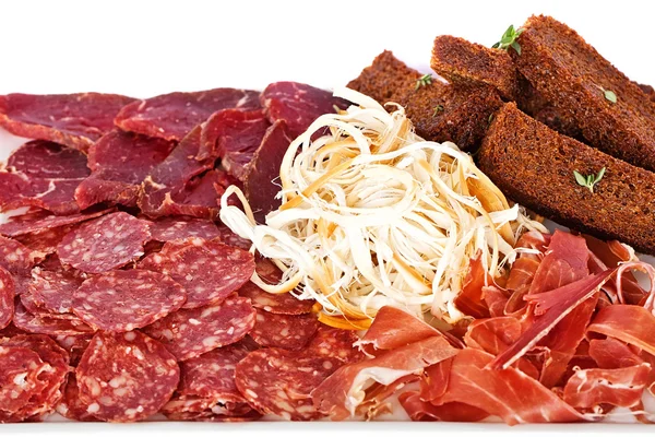 Meat appetizer. Salami, cured meat, toasted black bread and herbs on a white plate — Stock Photo, Image