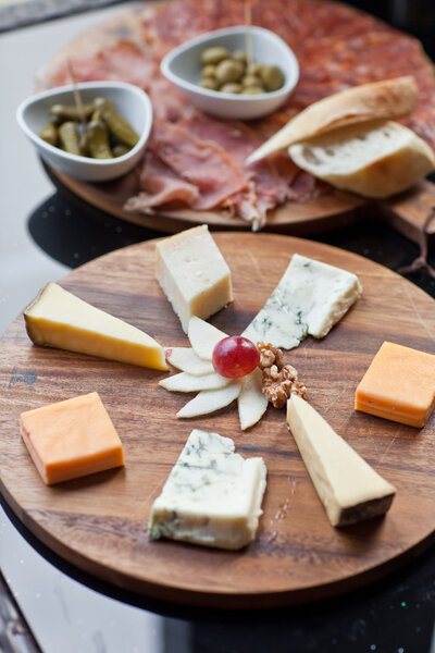 Wine appetizers set: meat and cheese selection, grapes and bread on a rustic wooden board over a dark wood background. Top view, copy space
