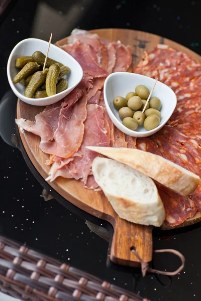Wine appetizers set: meat and cheese selection, grapes and bread on a rustic wooden board over a dark wood background. Top view, copy space — Stock Photo, Image