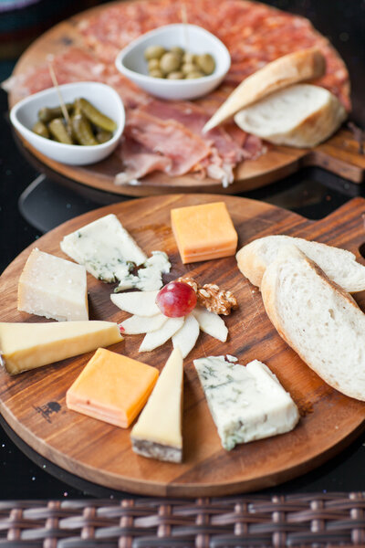 Wine appetizers set: meat and cheese selection, grapes and bread on a rustic wooden board over a dark wood background. Top view, copy space