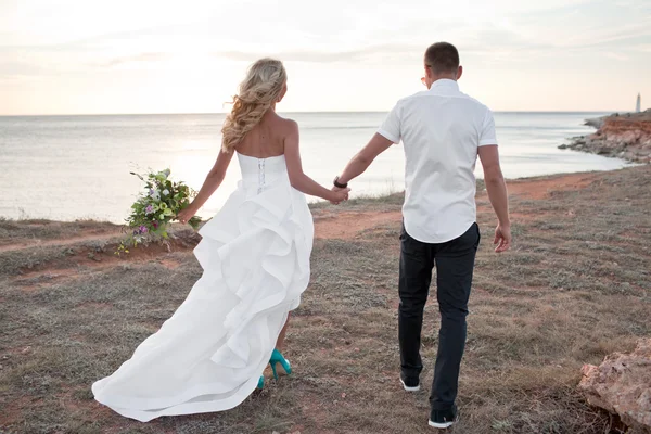 Elegante prachtige bruid en bruidegom lopen in de zonsondergang op de backgr — Stockfoto