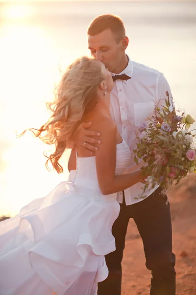 Elegante prachtige bruid en bruidegom lopen in de zonsondergang op de backgraund — Stockfoto