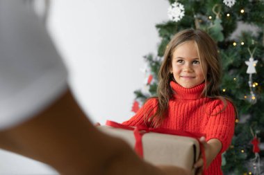 Avrupalı görünümlü bir kız kırmızı kazak giyiyor. Bir kadının elinden hediye alır.