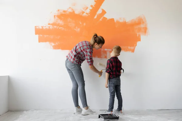 A mãe e o filho estão a pintar a parede com tinta laranja. conceito de renovação de casa — Fotografia de Stock