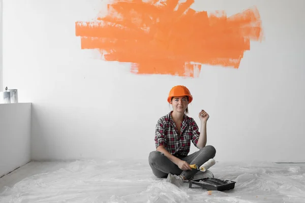 Mulher feliz senta-se no chão com mancha laranja na parede. conceito de renovação de casa — Fotografia de Stock